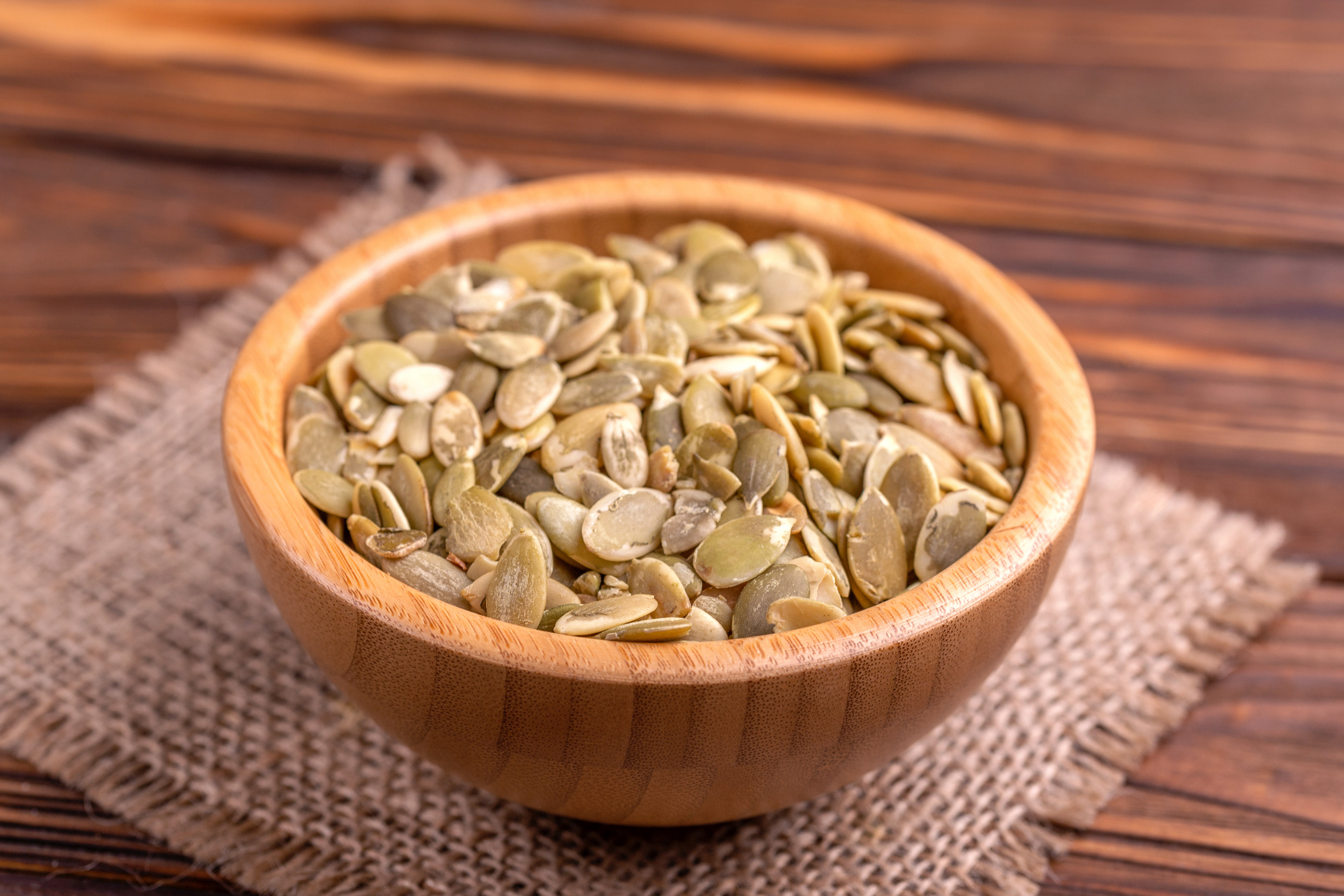 Fresh pumpkin seeds in wooden bowl with burlap napkin on wooden background. Copy space. Horizontal view