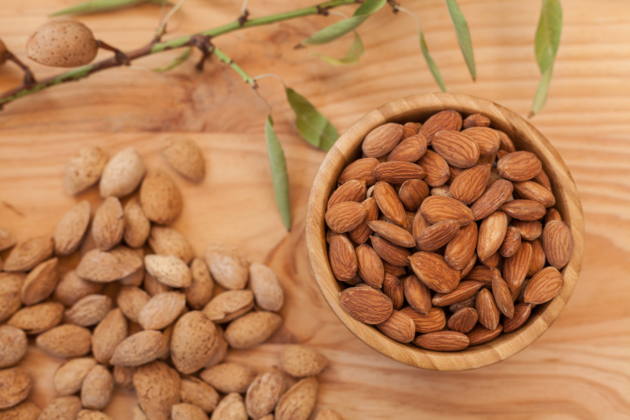 Top view of shell and peeled almonds in wooden bowl and on wooden table with a unfocussed almond tree branch