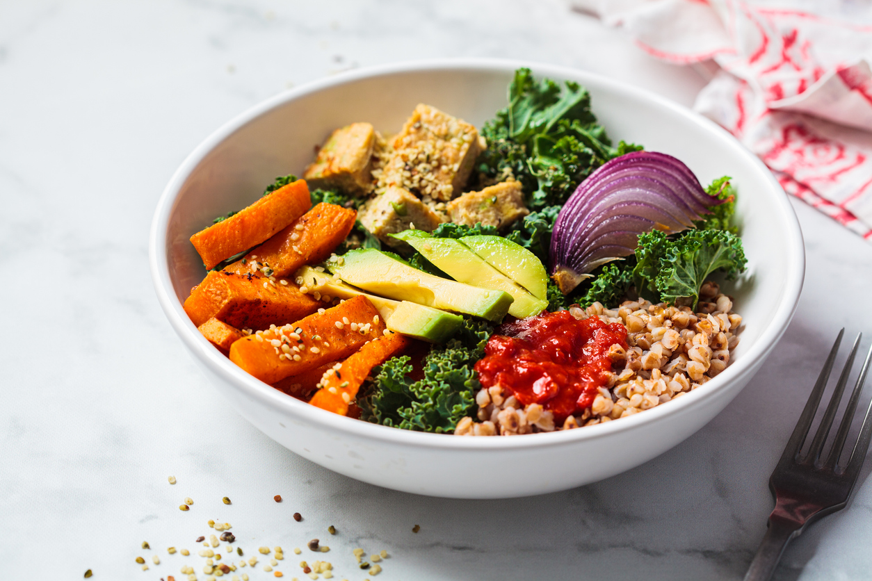 Baked vegetables, avocado, tofu and buckwheat buddha bowl. Vegan lunch salad with kale, baked sweet potato, tofu, buckwheat and avocado in a white bowl. Vegan concept.