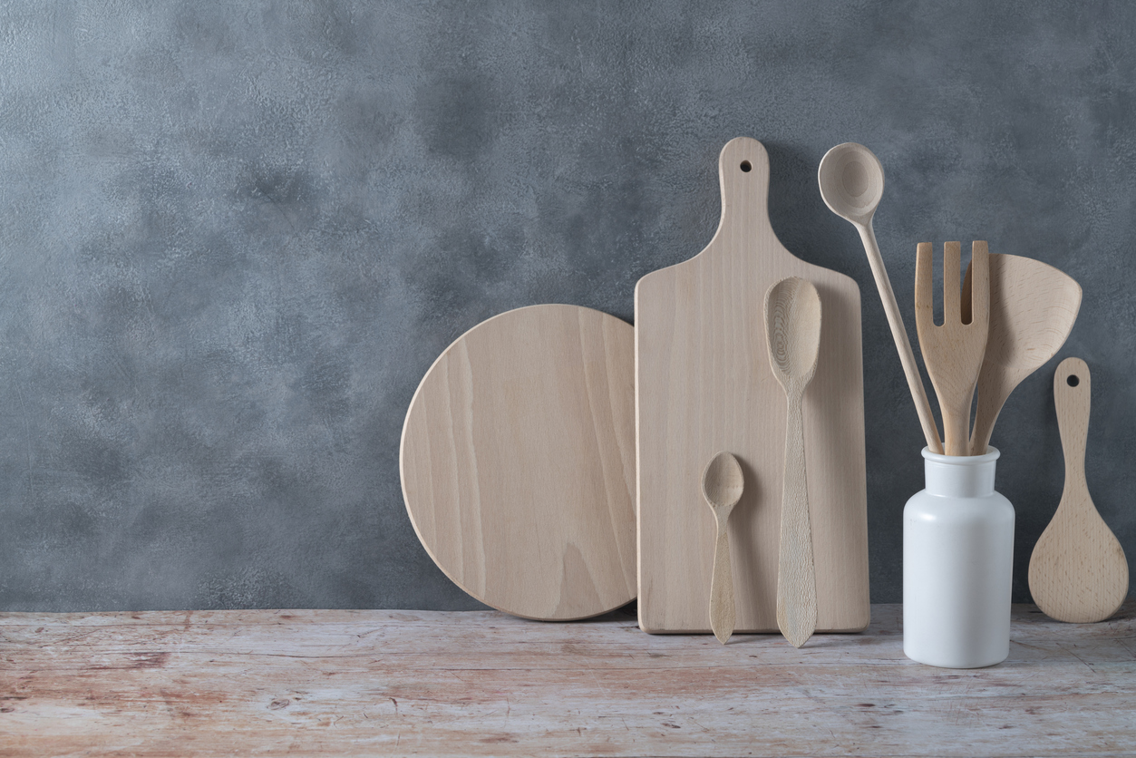 Modern kitchen kitchenware in light wood color with ladle, cutting boards and cookware on contemporary gray cement wall