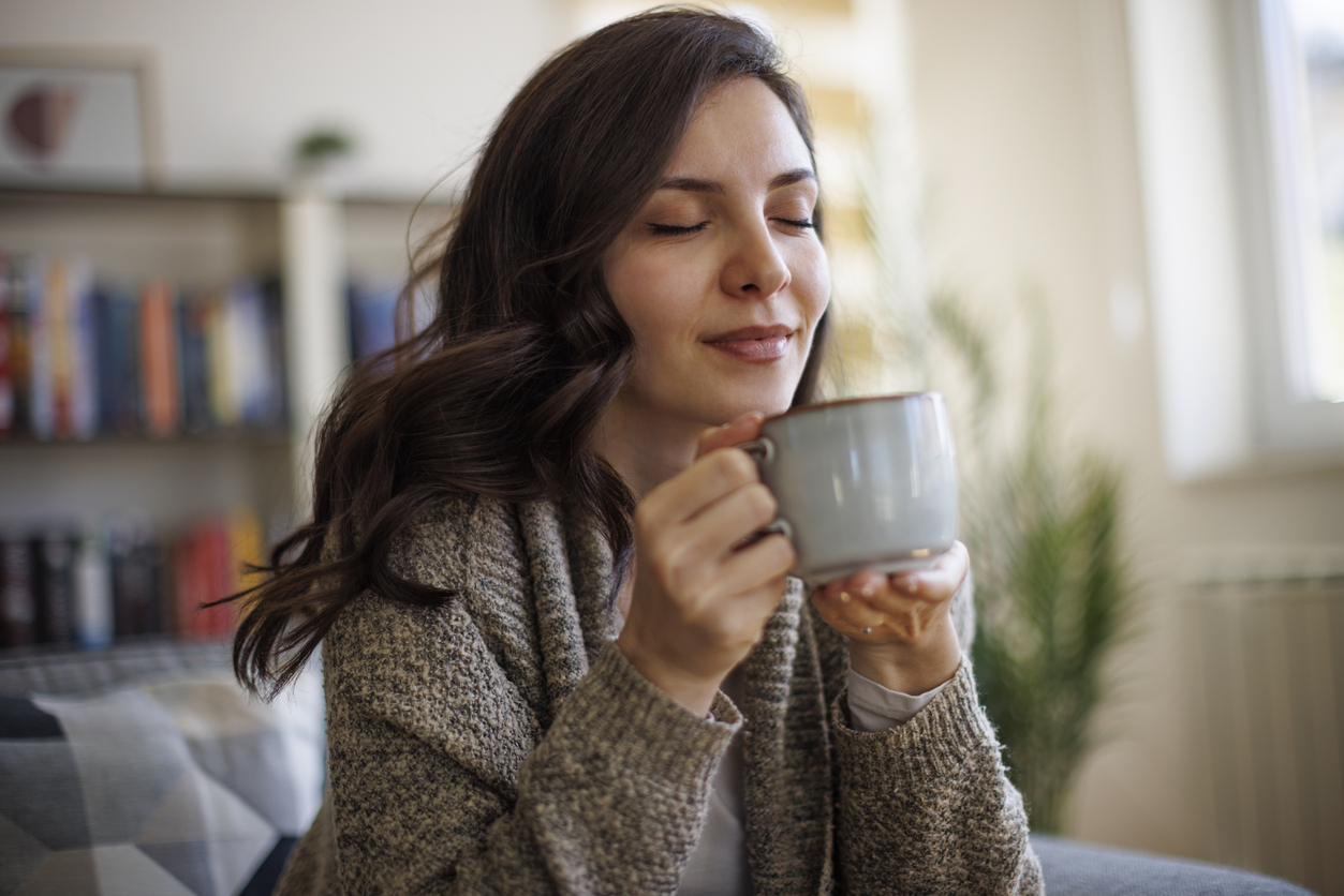 Young smiling woman enjoying in smell of fresh coffee at home