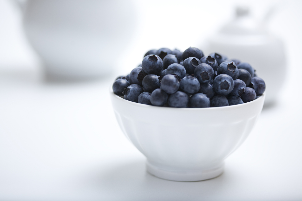 Heap of fresh blueberries in a white bowl with white objects in a white background with available copy space.