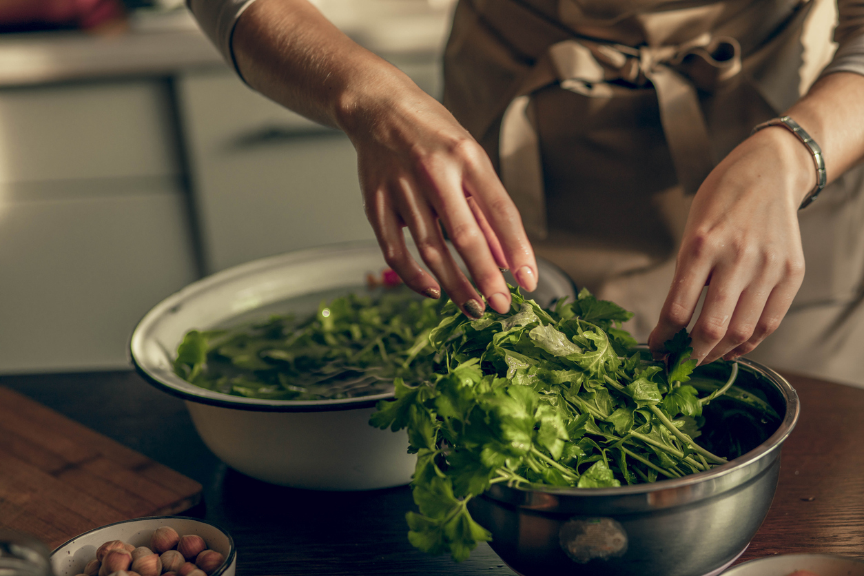 hands of a young woman in the kitchen is washing parsley greens for a vegan morning
