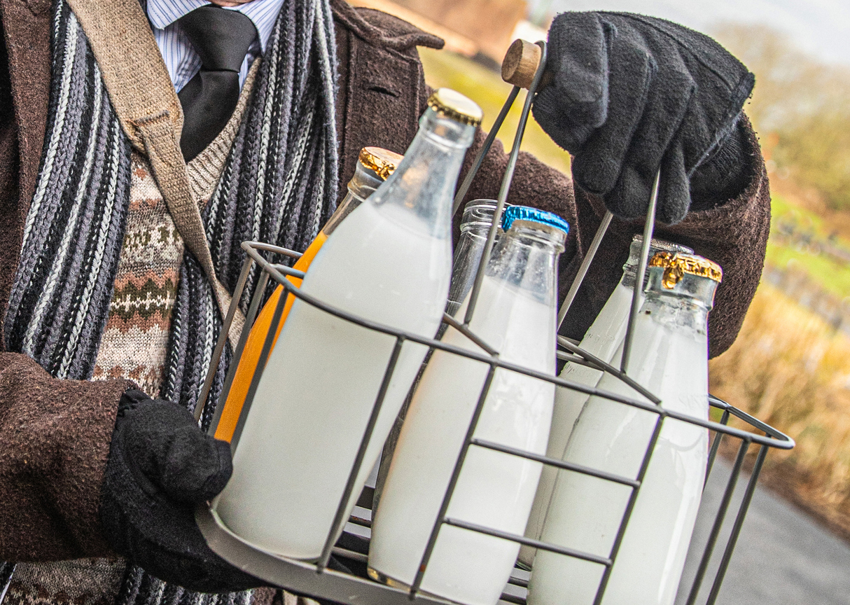 Old fashioned milkman with bottles of milk of different varieties held in a metal bottle holder - this is how milk was delivered in earlier years