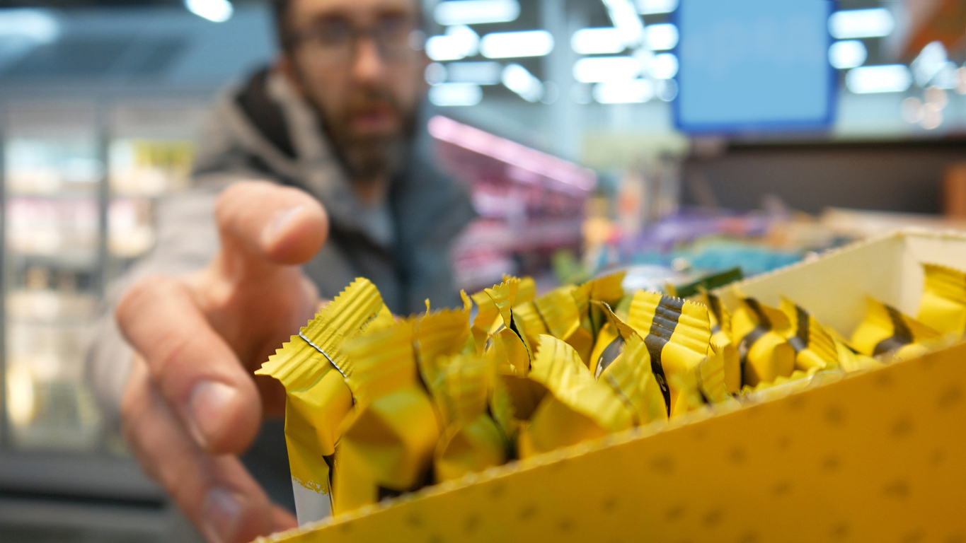 A man reaching the hand to take a protein bar from a supermarket shelf close-up
