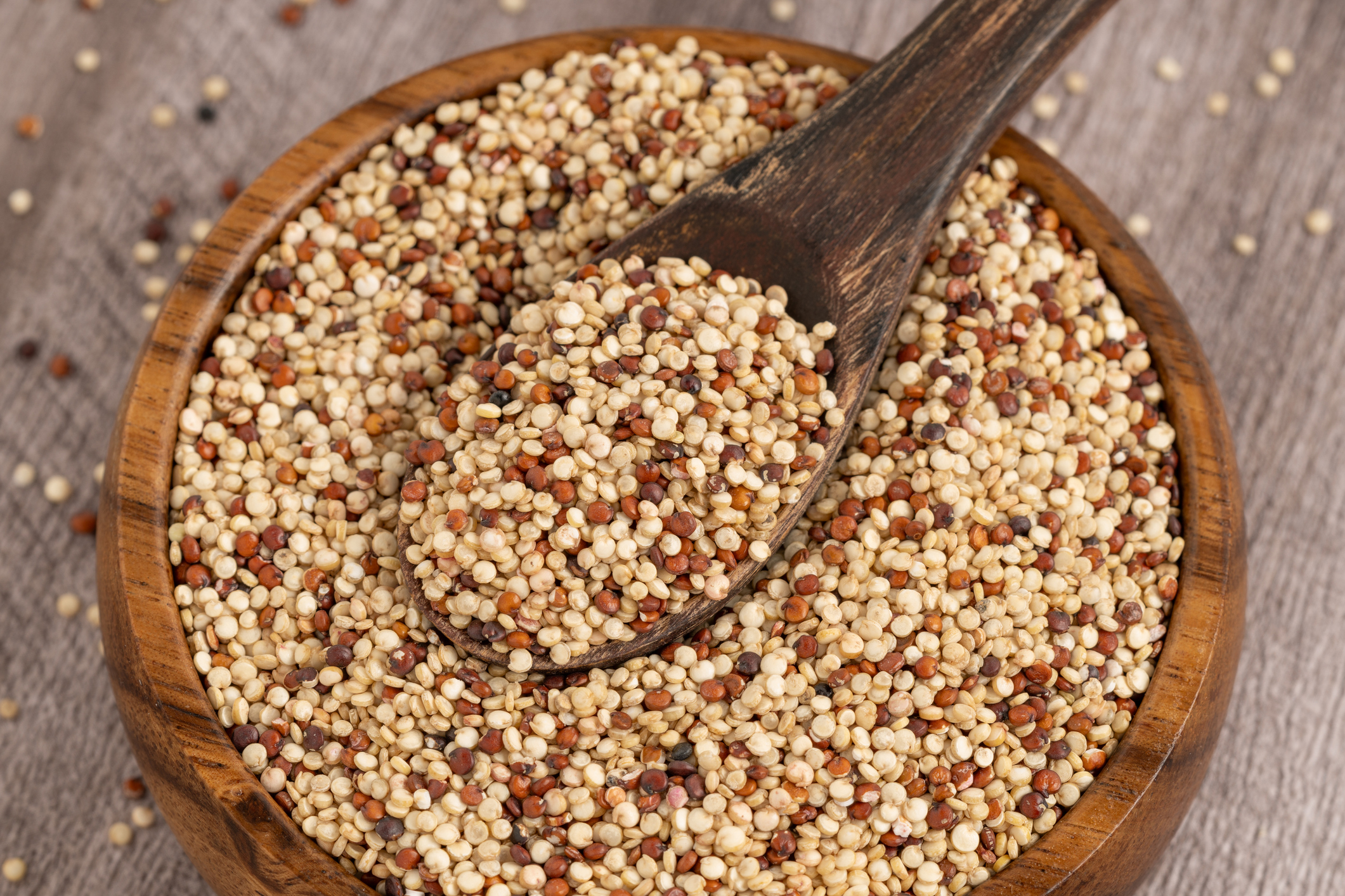 A close-up of mixed quinoa grains in a wooden bowl with a spoon, placed on a wooden surface. A nutritious superfood ideal for a healthy diet.