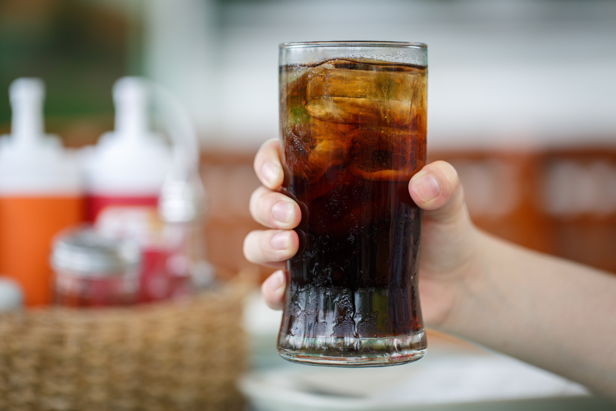 Hand holding glass of cola drink in restaurant background